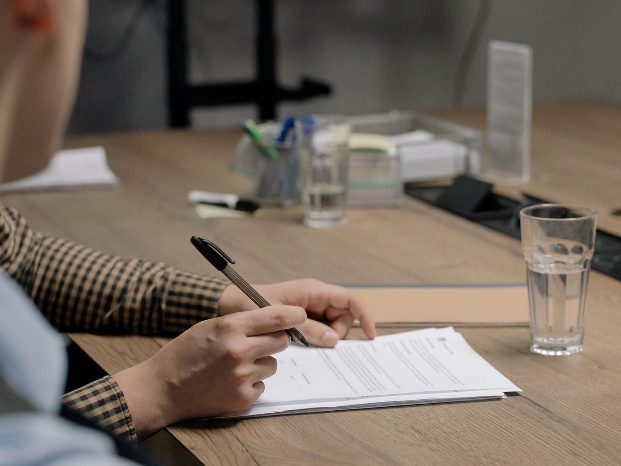 Manos firmando un documento sobre una mesa de reunión